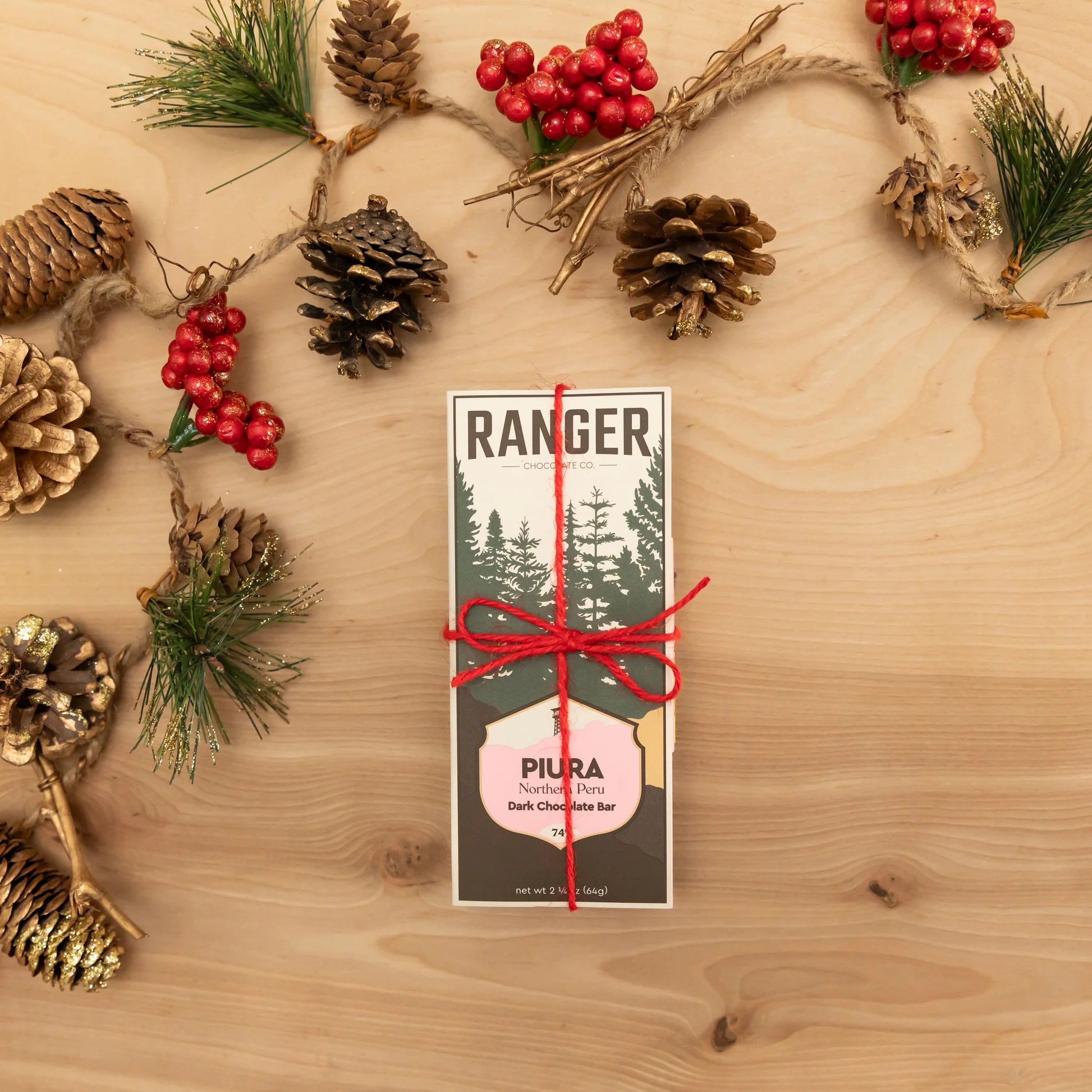 A Ranger Chocolate Co. bar wrapped with red twine among greenery and pinecones