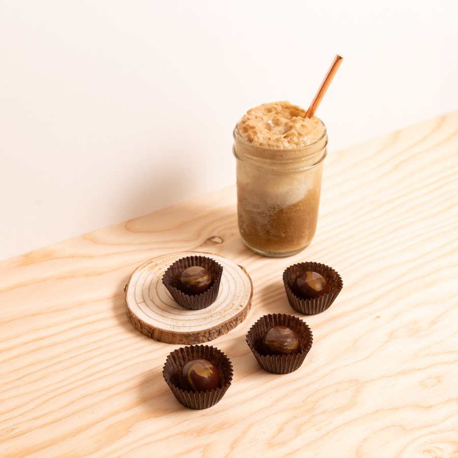 Chocolate root beer bonbons in brown paper cups beside a jar of root beer float on a wooden table